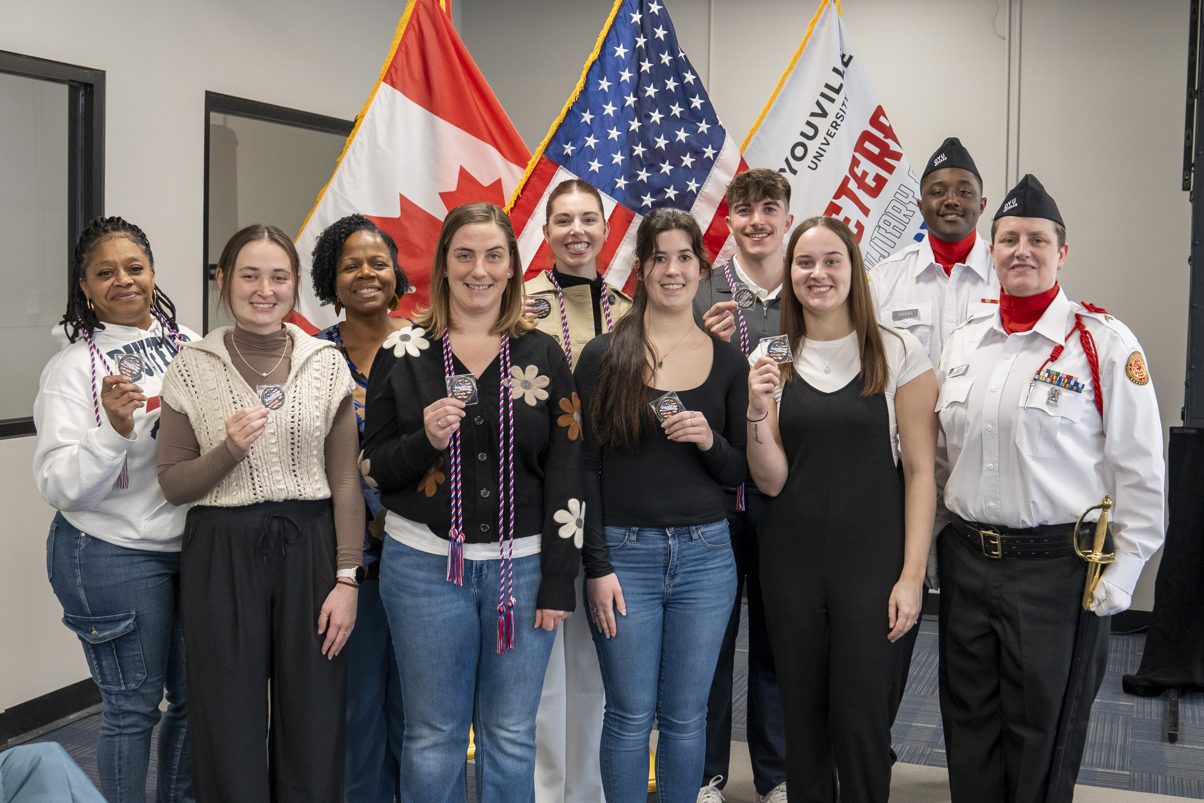 group of people stand together holding up a coin of excellence smiling at the camera