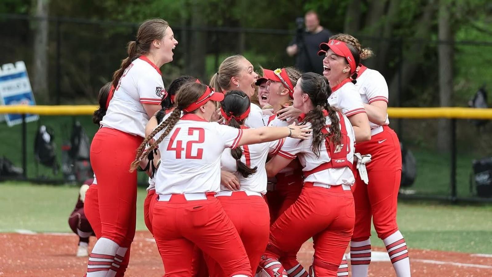 group of d'youville university softball players jumping up and down together in a group hug