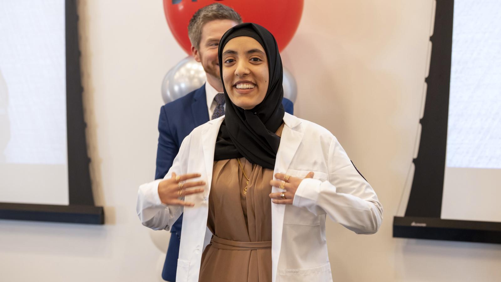 woman stands smiling at camera with white coat on