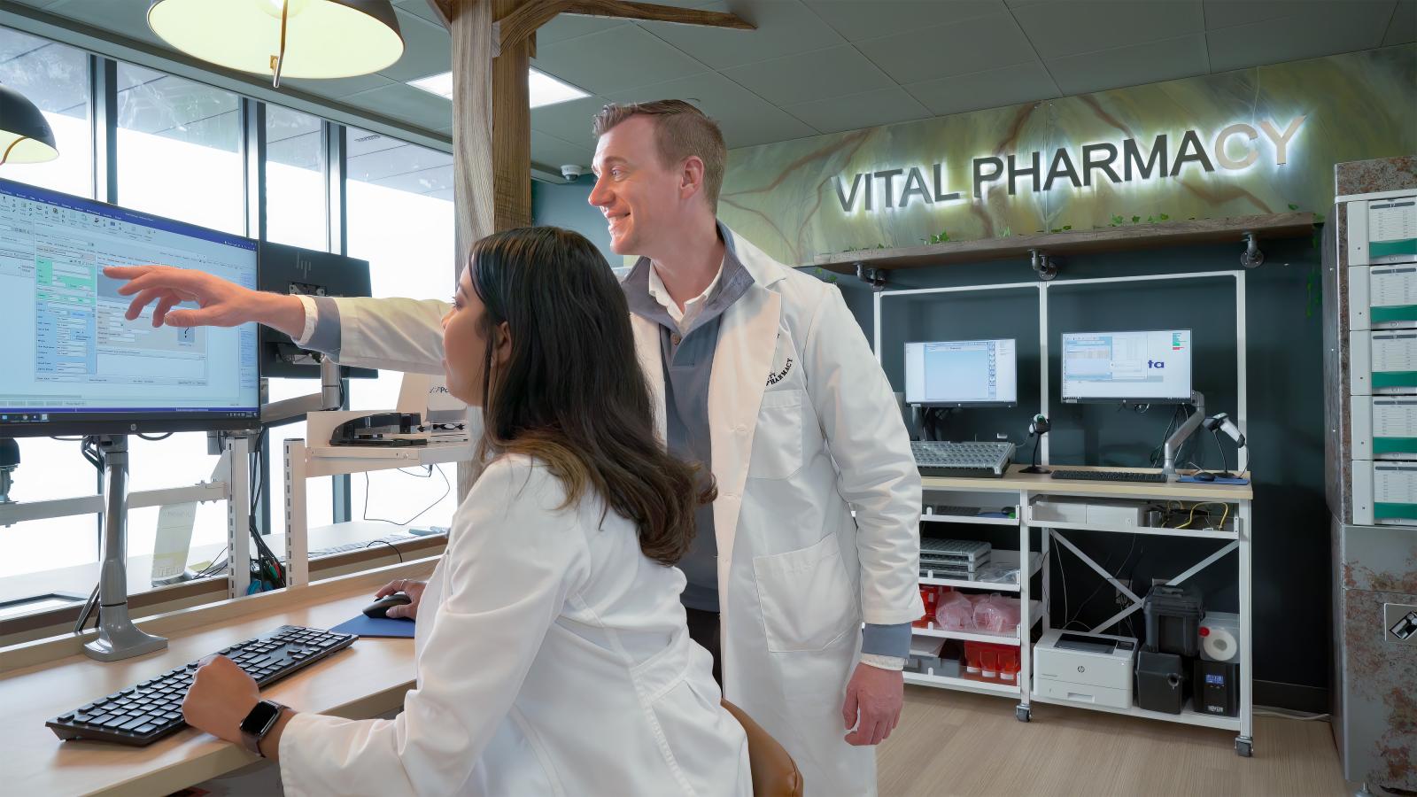 inside pharmacy. One person is pointing to a screen andother is typing on a keyboard