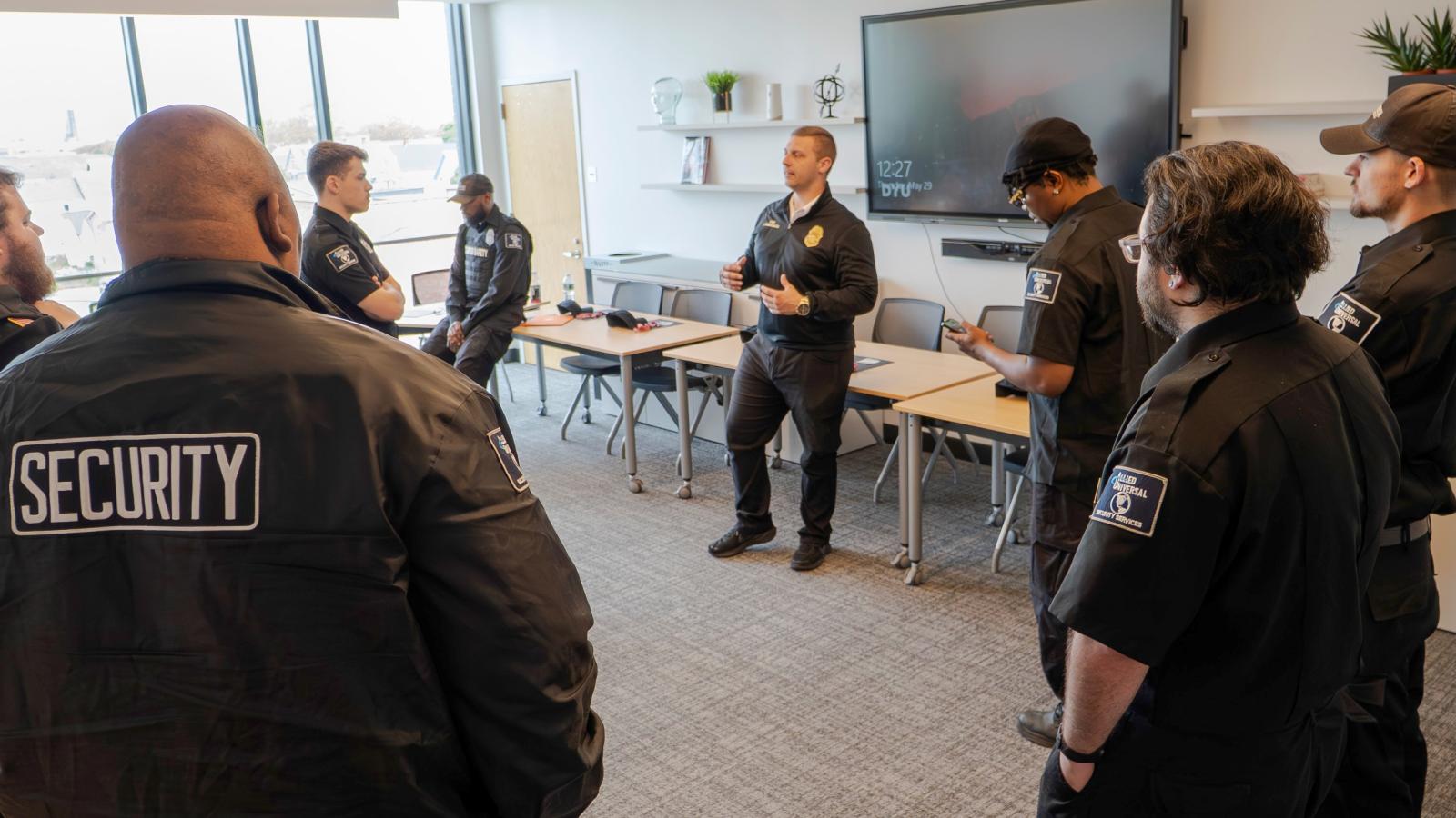 A group of campus safety officers stand in a circle. They are listening to one officer speak.