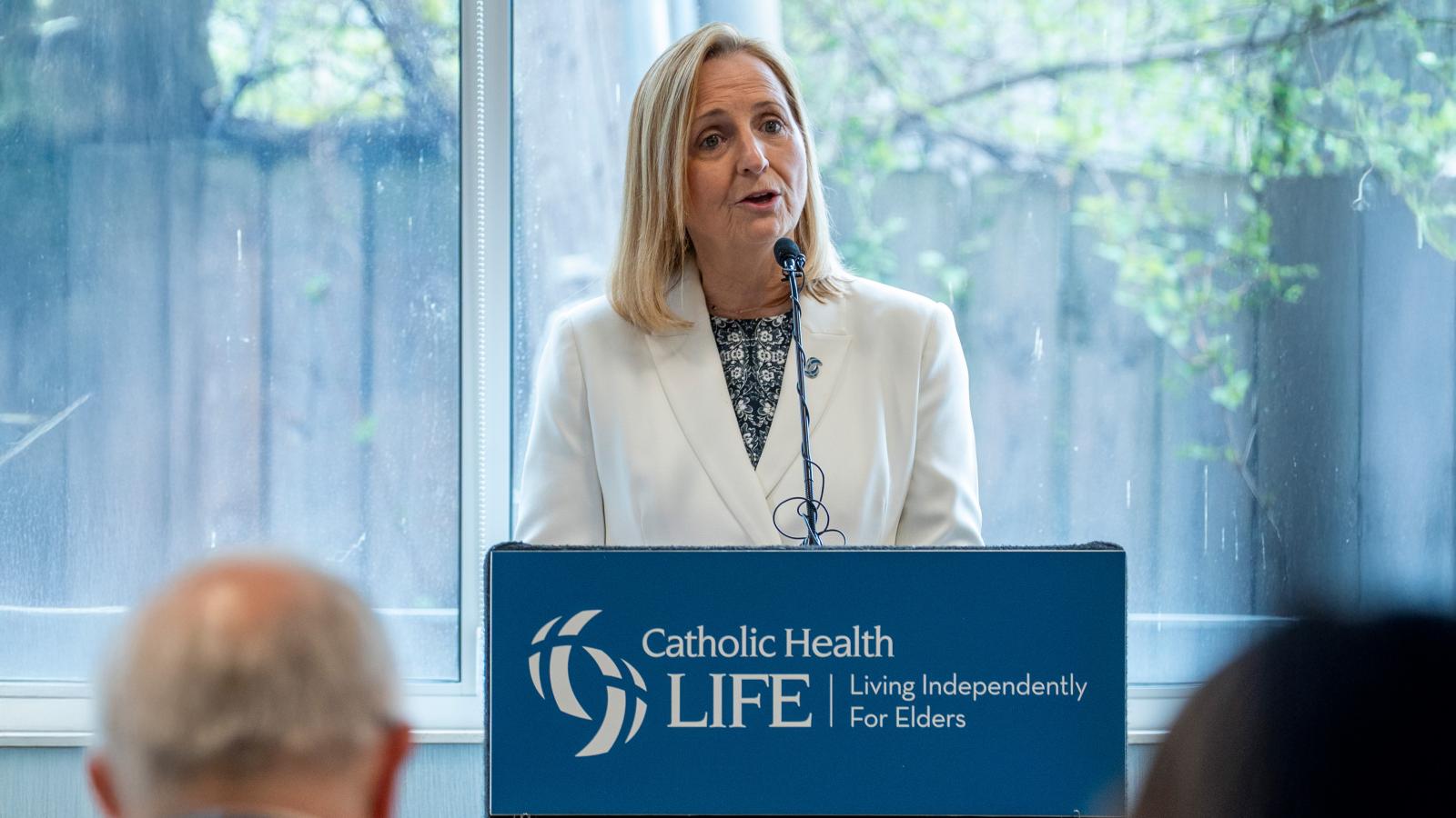 Joyce Markiewicz stands at a podium addressing an audience