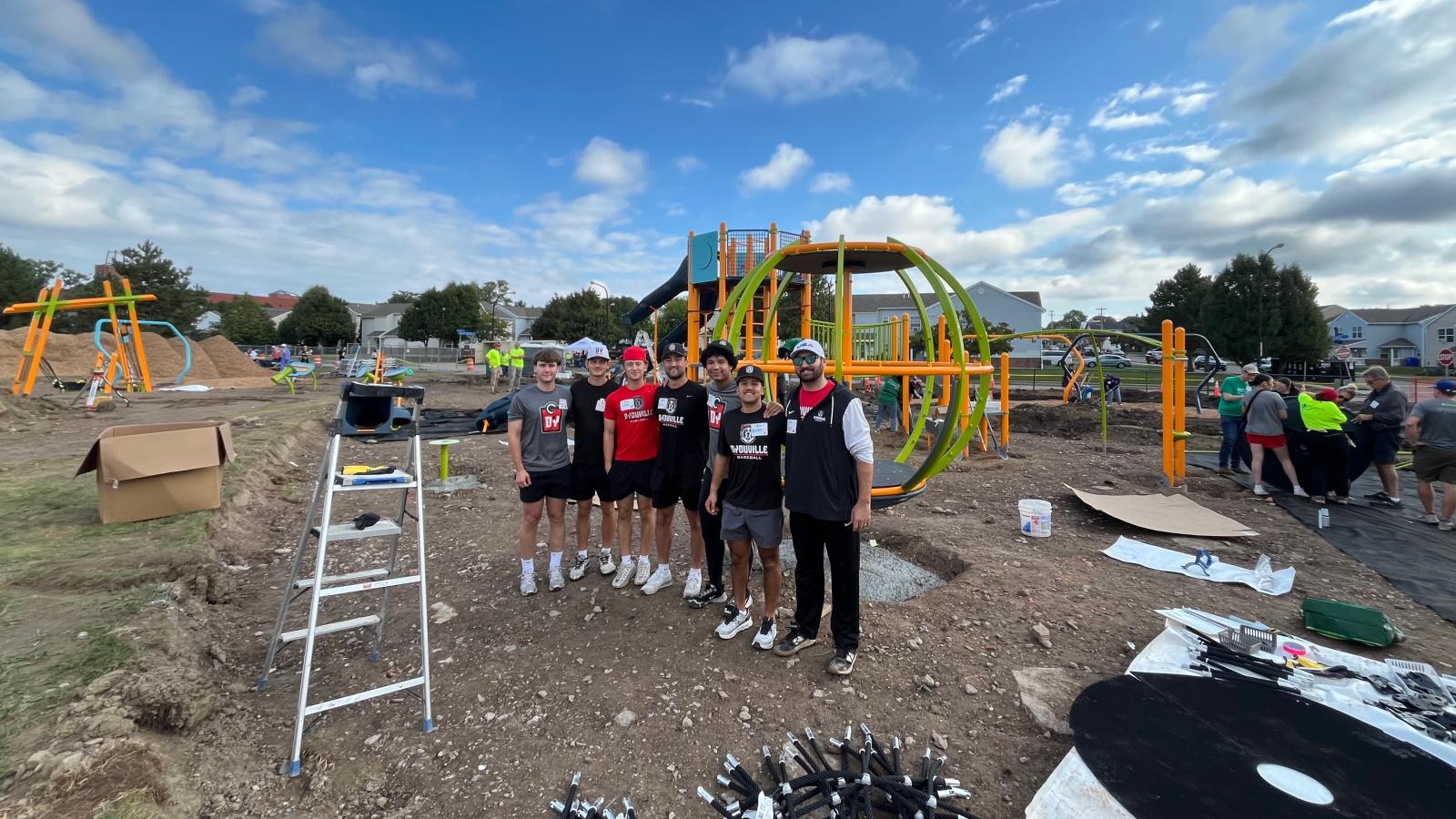 group of people stand smiling at the camera in front of a playground under construction