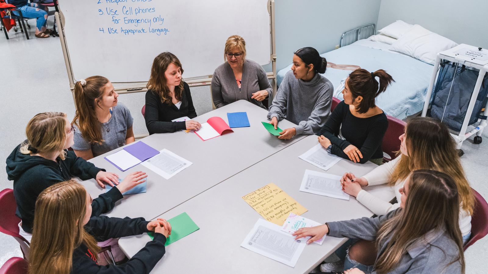 A group of women are seated in a circle around two rectangular tables
