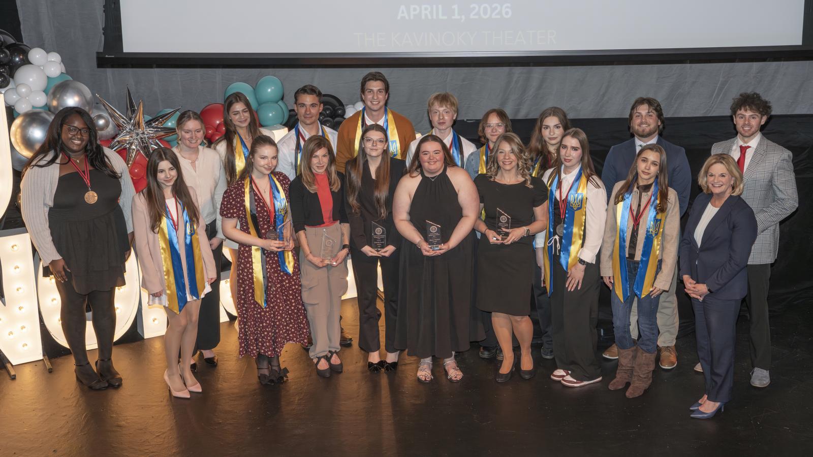 photo of large group of students smiling at the camera while standing on a stage