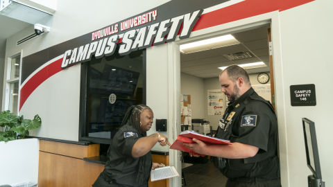 Two campus safety officers discussing paperwork in front of the main dispatch center