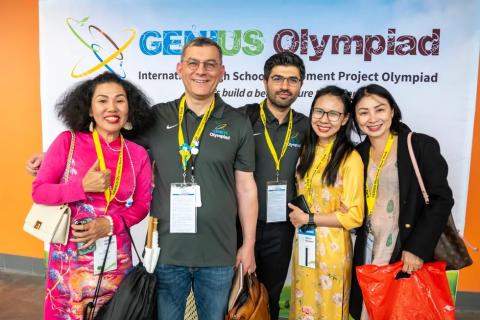 Dr. Fehmi Damkaci stands with four people in front of a Genius Olympiad backdrop