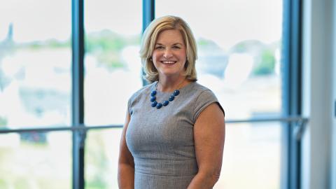 Lorrie Clemo PhD stands in front of a set of windows inside the Health Professions Hub
