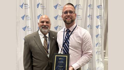 Dr. Matthew Smith DPT stands holding his award and smiling at the camera with another APTA member