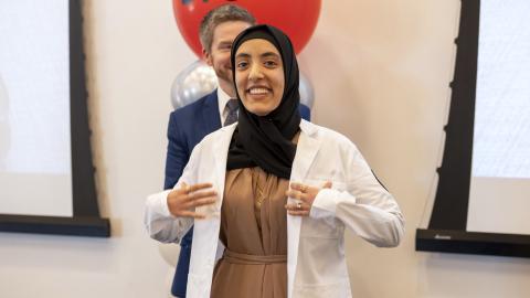 woman stands smiling at camera with white coat on