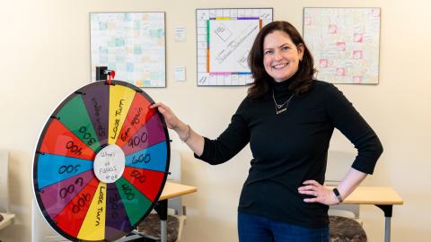 Clara Voorhees standing with a countertop prize wheel. three board games displayed on wall behind.