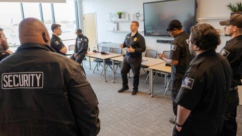 A group of campus safety officers stand in a circle. They are listening to one officer speak.