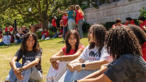 large group of students sitting outside in the grass talking and laughing