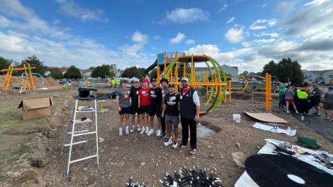 group of people stand smiling at the camera in front of a playground under construction