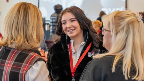 young woman stands smiling during a conversation with two other women