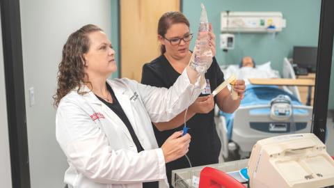 Shannon McCory-Churchill stands in simulation lab holding IV fluid
