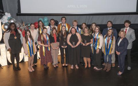 photo of large group of students smiling at the camera while standing on a stage