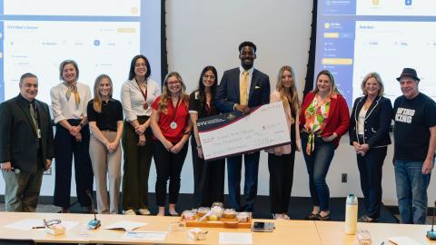 group stands in a row smiling at the camera. One stands holding an oversized check.