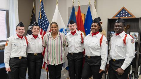 six individuals stand in front of US military and United States flags