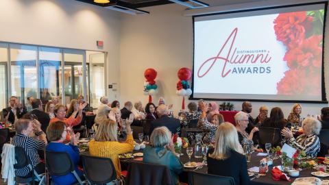 Projector screen that reads: Distinguished Alumni Awards, in foreground you see people sitting at tables for dinner