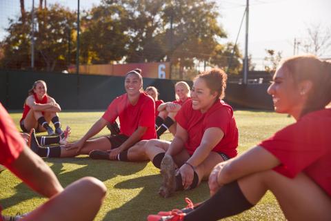 group of soccer players sitting on a field stretching and laughing