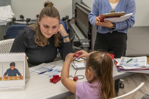 An occupational therapy student guides a young girl through a block-stacking activity in a pediatric skills lab.