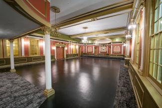 Large converted chapel with stage, balcony, and ornate early 1900s trimwork.