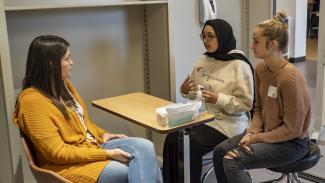 Three women sit at a table, one is currently speaking to the women seated across from her.