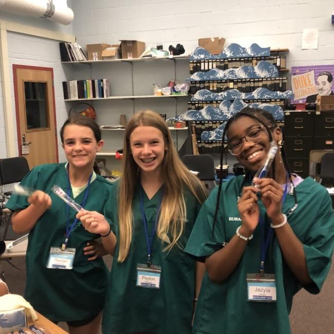 Three female students posing for the camera holding toothbrushes