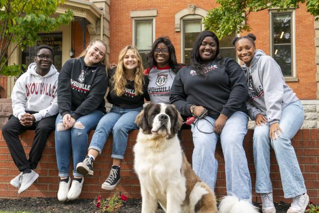 A group of six students sit on a brick wall with St. Bernard dog "Maggie".