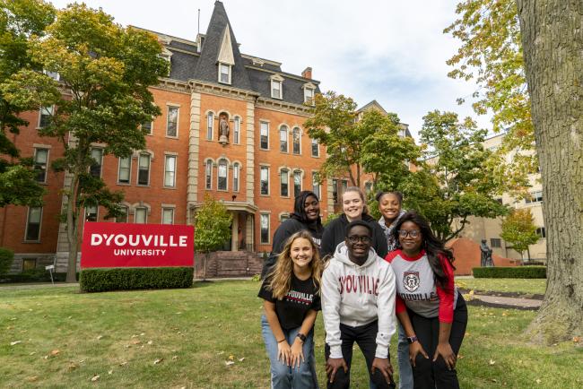 A group of six students pose in front of D'Youville University's original building - The Koessler Administration Building.