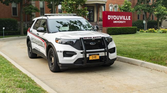 D'Youville University Patrol Vehicle parked in front of the D'Youville University sign in front of the Koessler Administration Building.