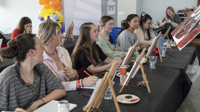 Group of students sitting at a table with easels painting.