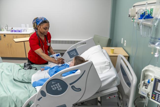 D'Youville University student takes the temperature of a actor patient in a simulation lab on campus