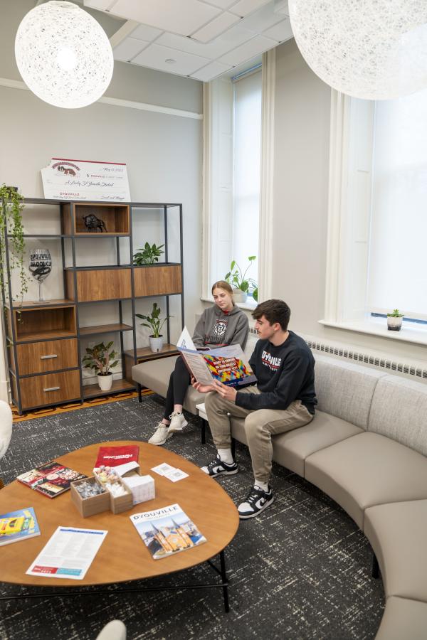 two students review a brochure while sitting on a couch.