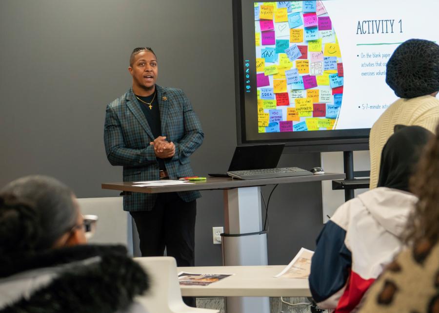 presenter stands at the front of a classroom next to a smartboard