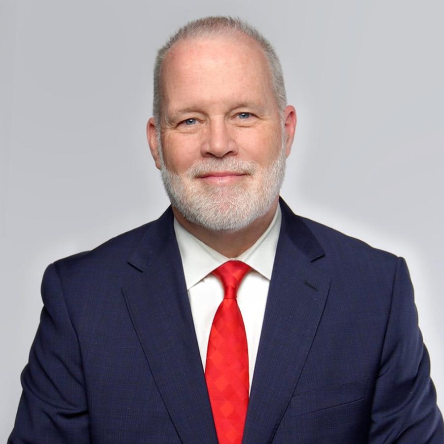 man in suit jacket and red tie smiles at the camera