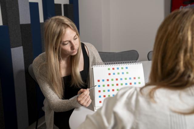 Woman points to a paper with many colored squares. You are looking over the shoulder of another woman.