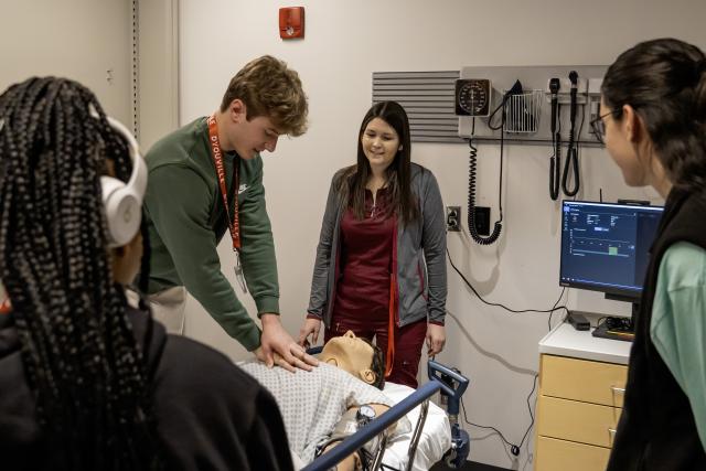 group stands around a manikin while one person performs cpr