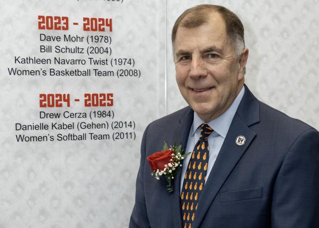 Drew Cerza stands with his name on the wall of D'Youville University Athletics Hall of Fame