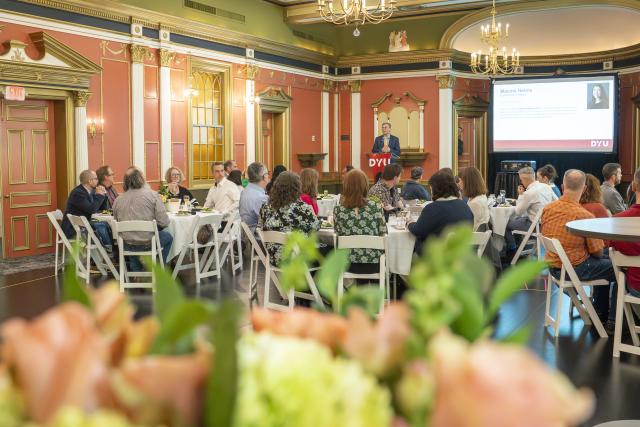 people sitting at round tables watching a speaker at a podium