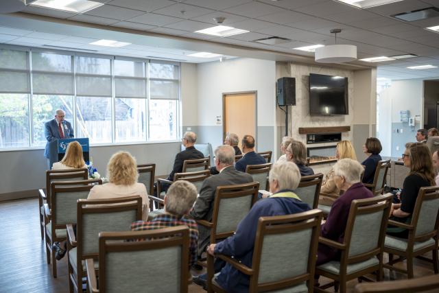 person stands at a podium address an audience seated in chairs