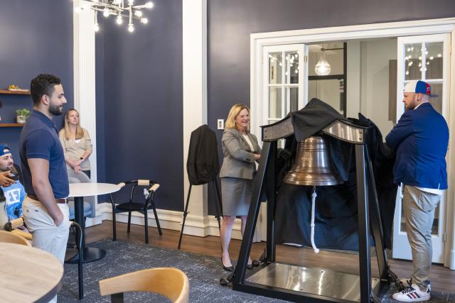 cover is removed from a large metal victory bell while a crowd watches