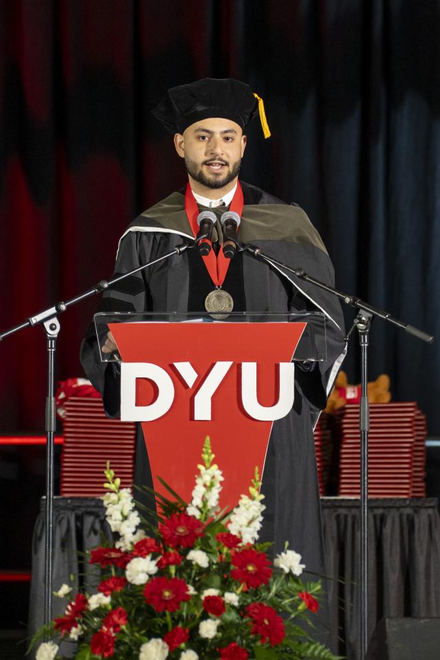 John rizk stands at podium reading his remarks