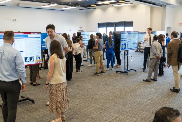 see large room with many posters and students speaking to visitors