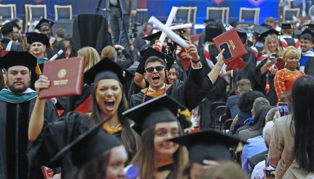 graduates recessing at commencement. graduates are holding up their degrees and cheering