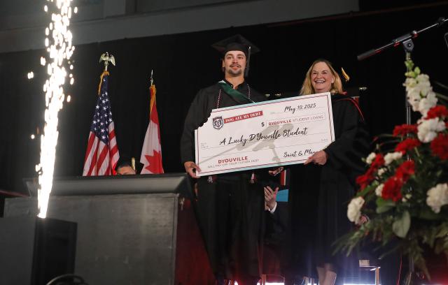 student stands with large check with president clemo
