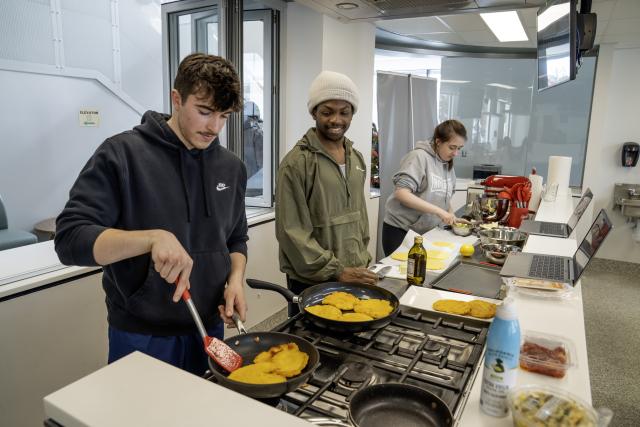 student is standing in the demonstration kitchen flipping food in a pan