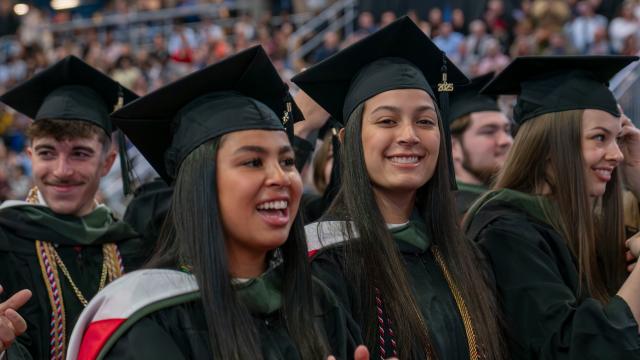 students in cap and gowns at a graduation ceremony smile at the camera