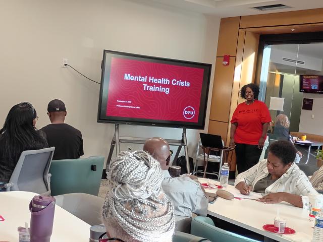 a person stands next to a screen with a powerpoint presentation in front of a group of people seated at tables
